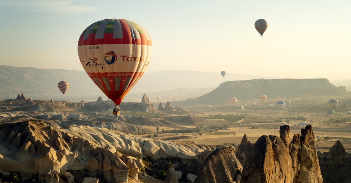 Breathtaking aerial view of hot air balloons floating over Cappadocia's unique rock formations at sunrise.