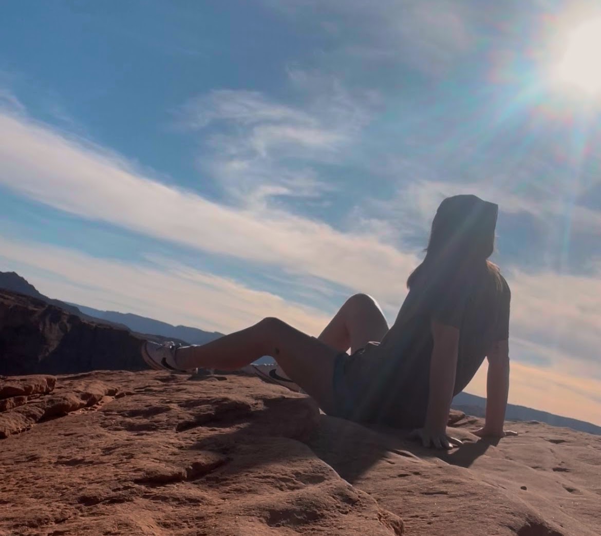 a girl sitting on the ground with back turned looking to the horizon