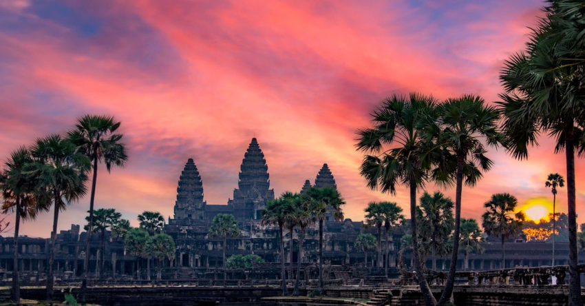 Breathtaking view of Angkor Wat in Cambodia at sunset, surrounded by palm trees.