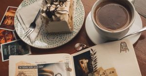 A cozy café setting with a slice of cake, cup of coffee, Polaroids, and an open journal.